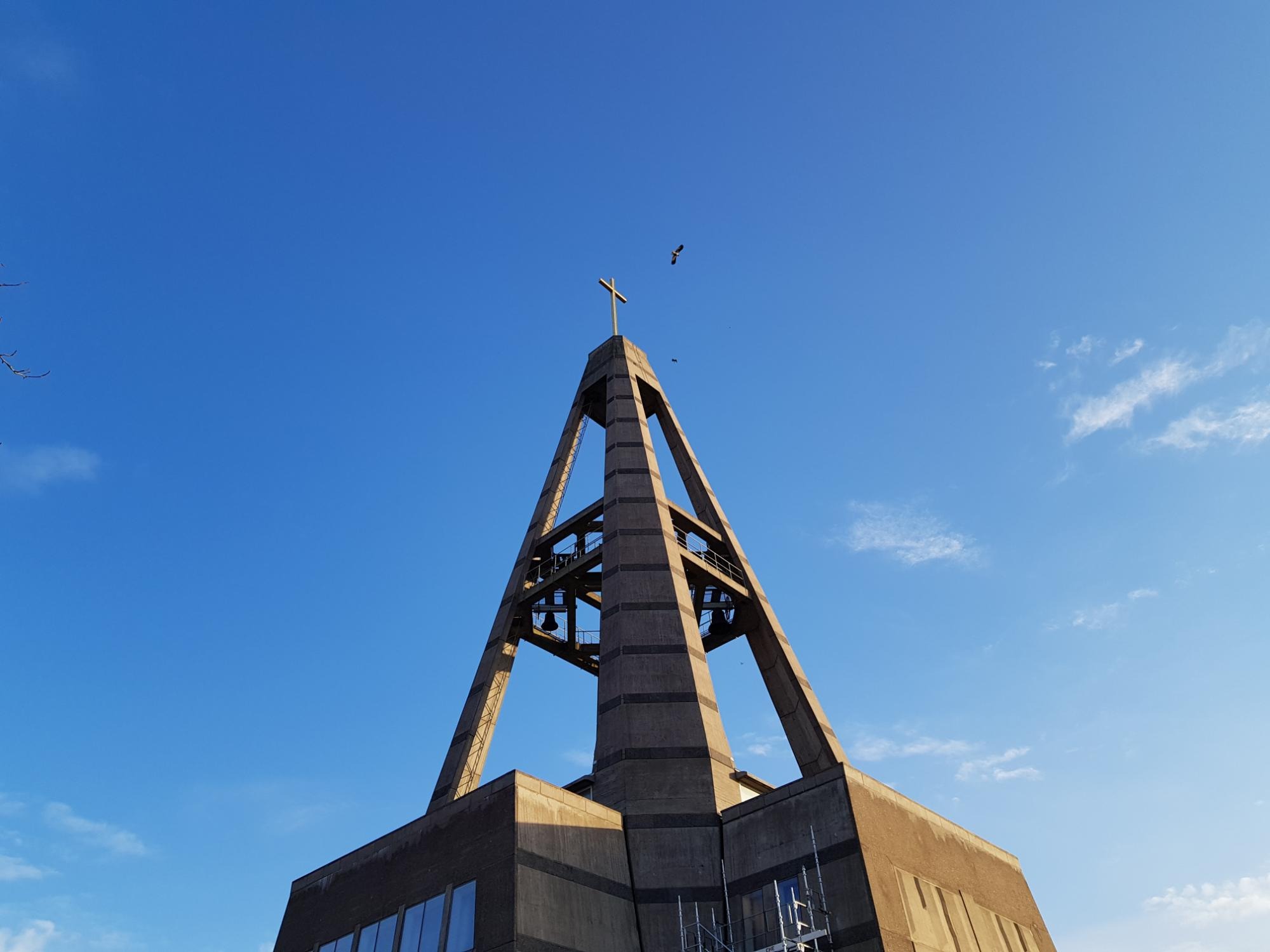 Kyrkan i betong och förgyllt kors mot blå himmel