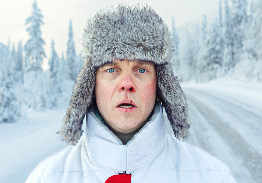 En person i vinterkläder i ett snölandskap tittar in i kameran med öppen mun och blod i näsan och på läppen.