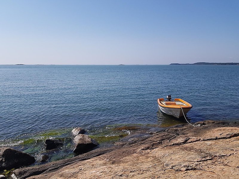 En motorbåt förtöjd vid en klippa med havet och horisont i bakgrunden.