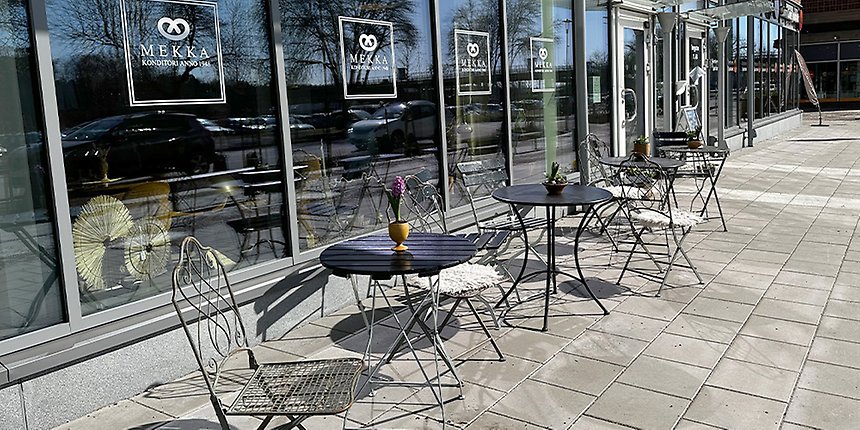 Cafémöbler utanför en lokal med texten Mekka på fönstren.