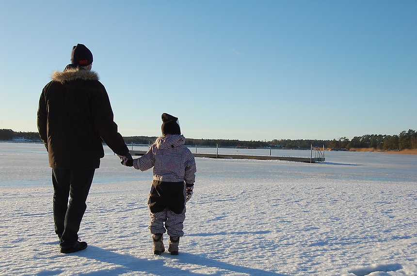 En vuxen och ett barn står i snön och håller handen.